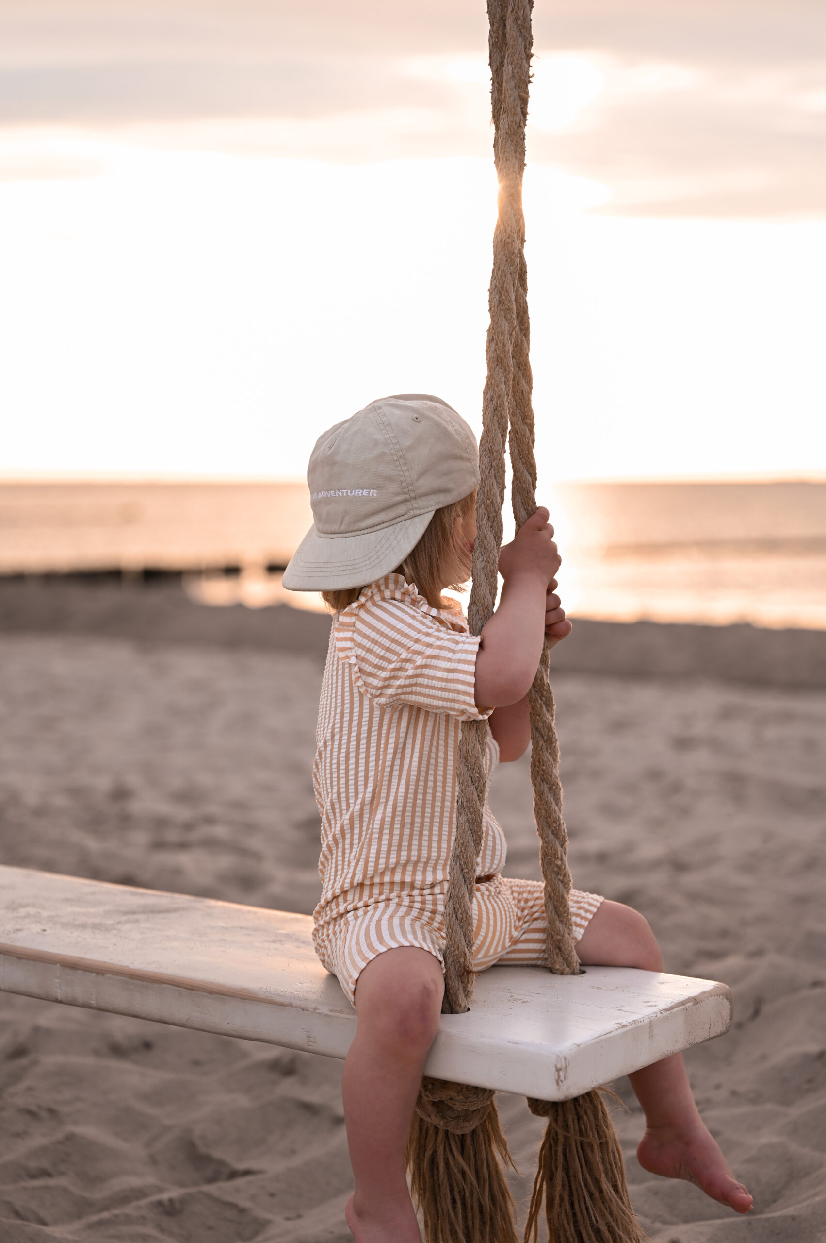 Ein kleines Mädchen auf einer Schaukel am Strand im Sonnenuntergang bei einem Familienshooting in Rostock