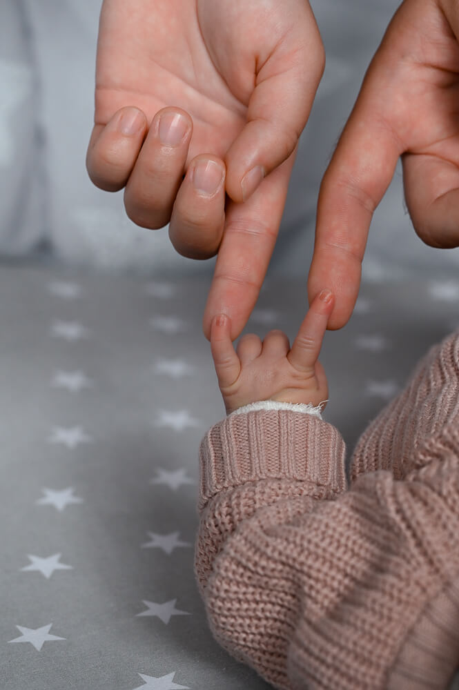 Die Hand eines Neugeborenen und die Finger von Mama und Papa bei einem Familienshooting mit Neugeborenem in Rostock
